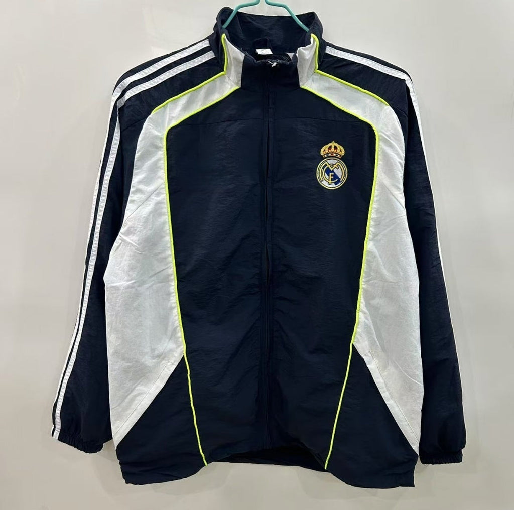 Veste coupe-vent réversible Real Madrid, marque Le 12 -ème Maillot, montrée pliée avec logo et détails de design.
