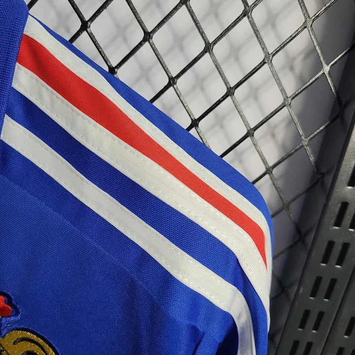 Maillot rétro de l'équipe de France 1985/86, modèle Le 12, avec design vintage et logo officiel, vue de face sur fond blanc.