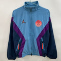 Veste coupe-vent réversible PSG bleue de la marque Le 12 -ème Maillot, avec logo Paris Saint-Germain visible.