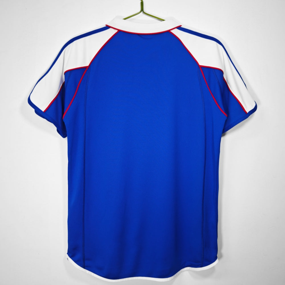 Maillot domicile rétro du Japon 2000, marque Le 12ème Maillot, en bleu avec logo de l'équipe nationale.