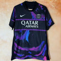 Maillot PSG 25/26 Le 12 -ème Maillot, maillot de football rouge avec logo du Paris Saint-Germain visible en détail