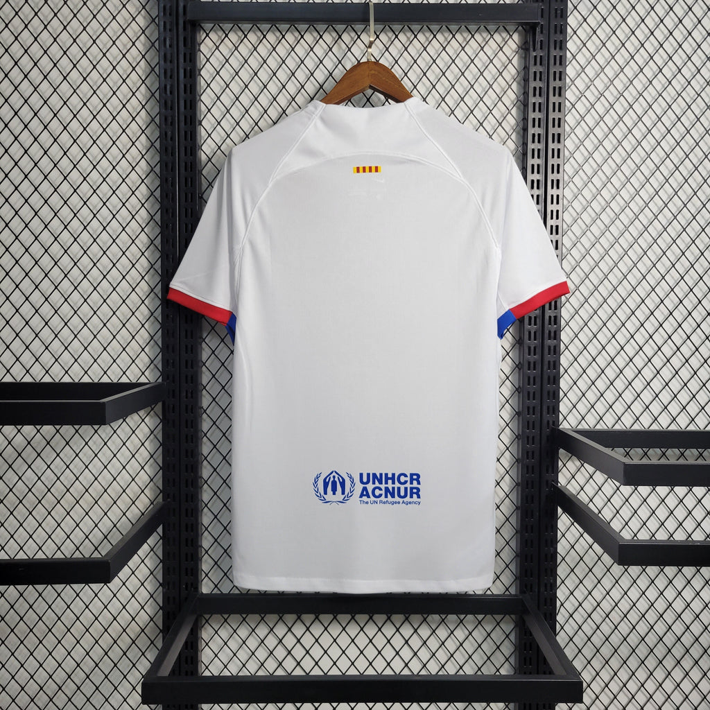 Maillot extérieur du FC Barcelone 2023-2024, marque Le 12, avec le logo du club et design bleu et grenat visible sur le maillot.