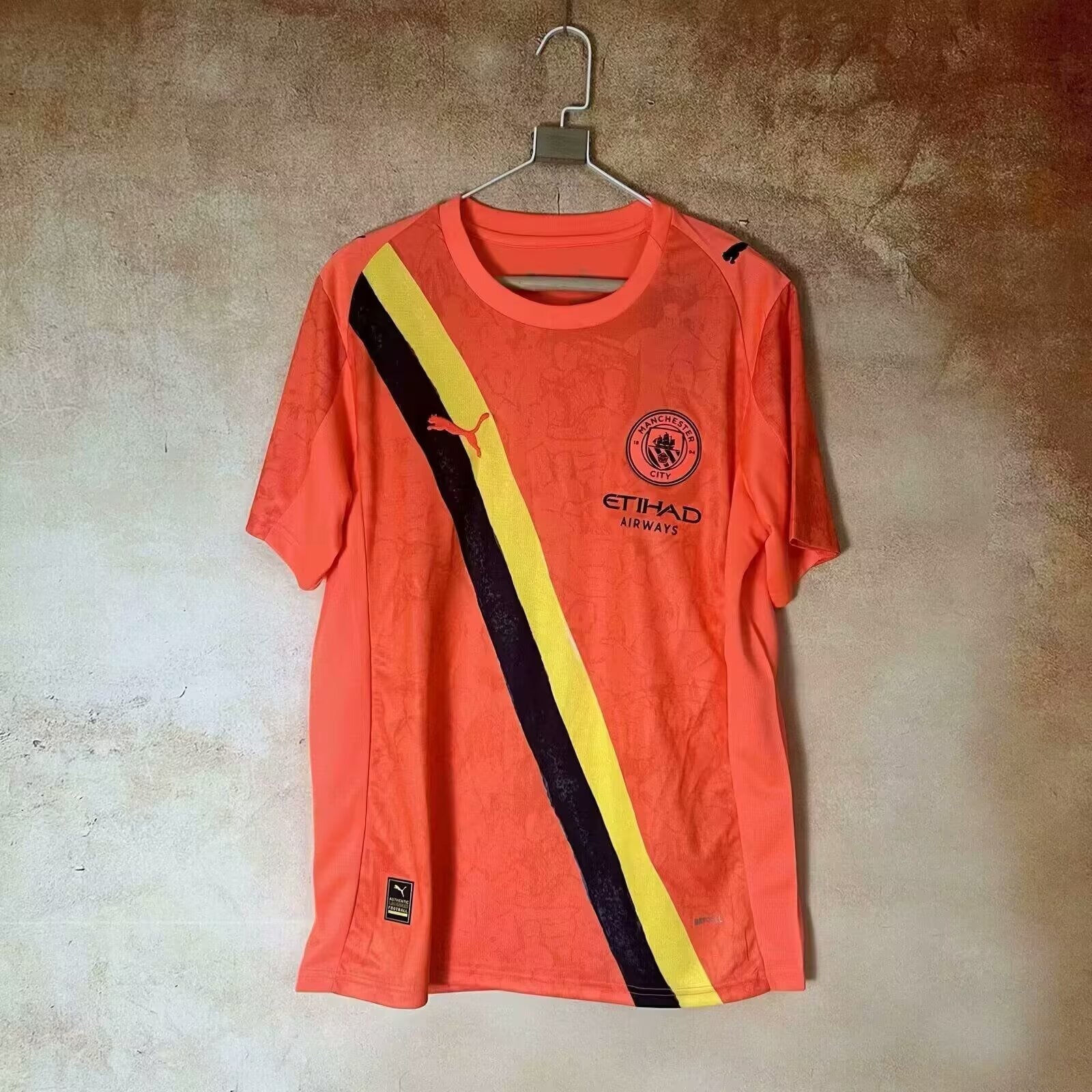 Maillot Manchester City 2025-2026, orange, en tissu léger, porté par un mannequin, avec logo et détails du club.