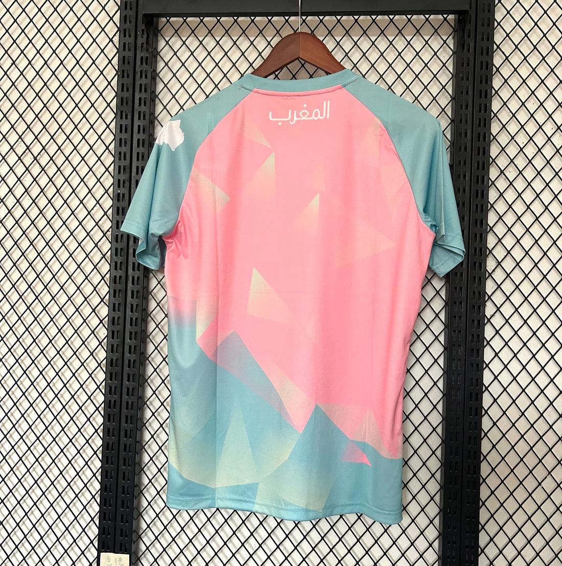 Maillot de football 25/26 Maroc Le 12 en turquoise, près du drapeau marocain, vue de face.