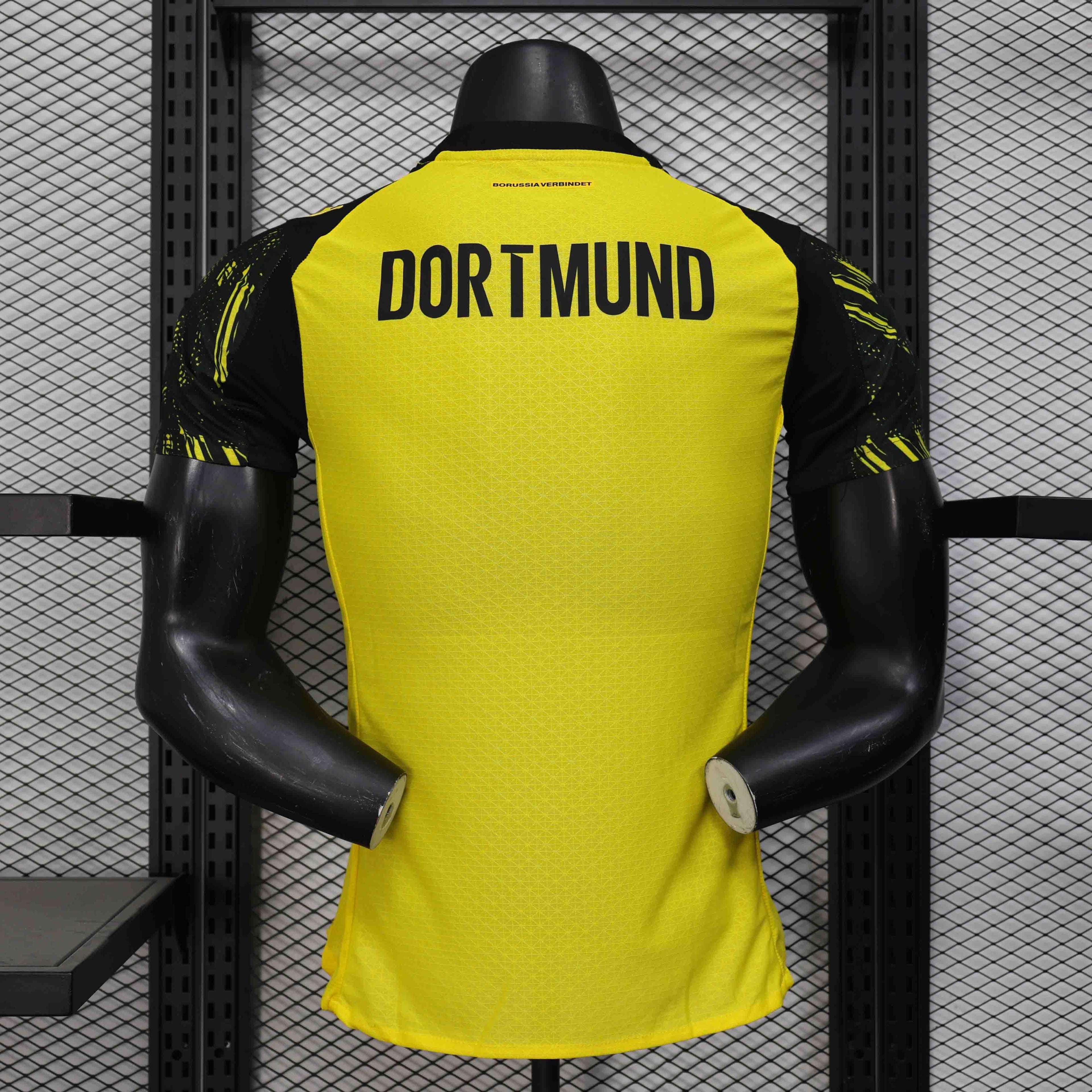Maillot Dortmund 25-26 Le 12 -ème Maillot, maillot de football noir avec logo et détails dorés, vue de face.