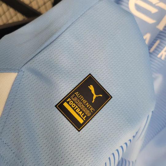 Maillot Manchester City 2023 2024 à manches longues, Le 12 -ème Maillot, logo et design bleu avec détails blancs visible.