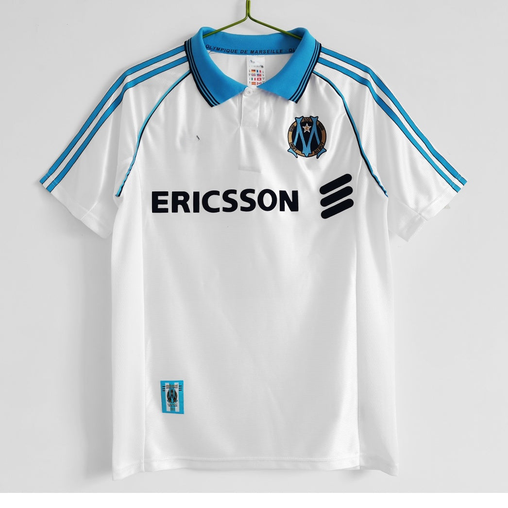 Maillot domicile rétro de l'Olympique de Marseille 1998-1999, marque Le 12-ème Maillot, vue de face avec détails du design.